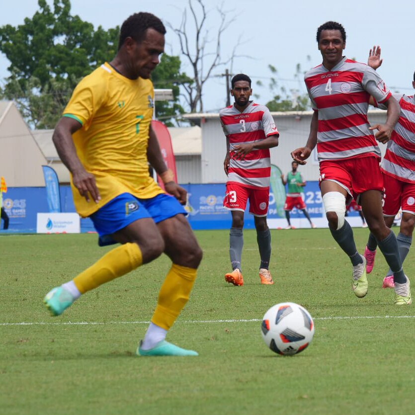 New Caledonian players run towards a Solomon Islands player who has the ball.
