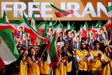 People wave flags with "Free Iran" written on screens in the background.