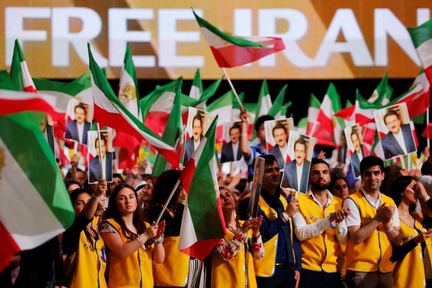 People wave flags with "Free Iran" written on screens in the background.