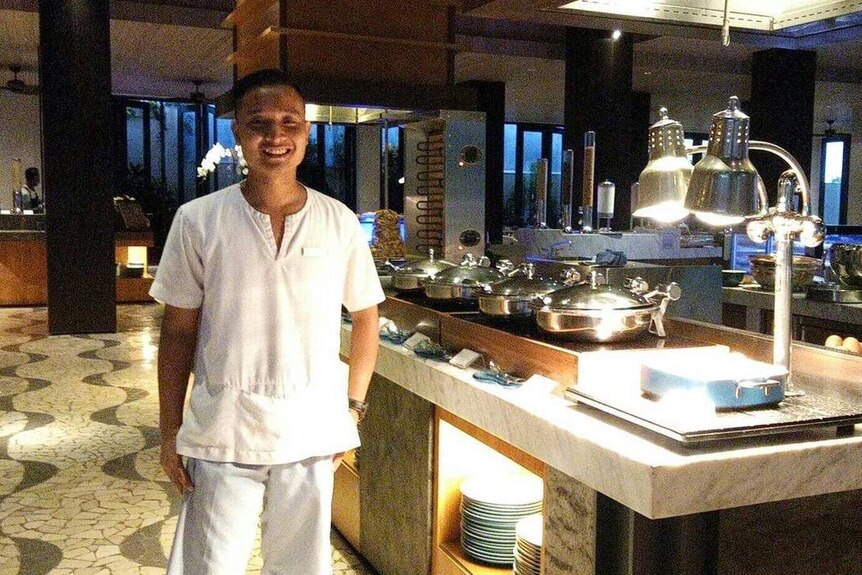 A picture of a man smiling standing in an empty hotel restaurant.