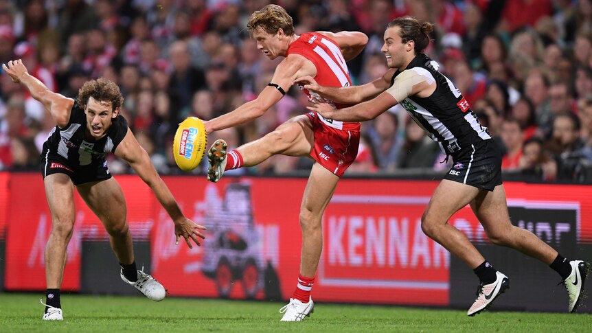 Callum Mills of the Swans gets a kick away despite pressure from Tim Broomhead of Collingwood.