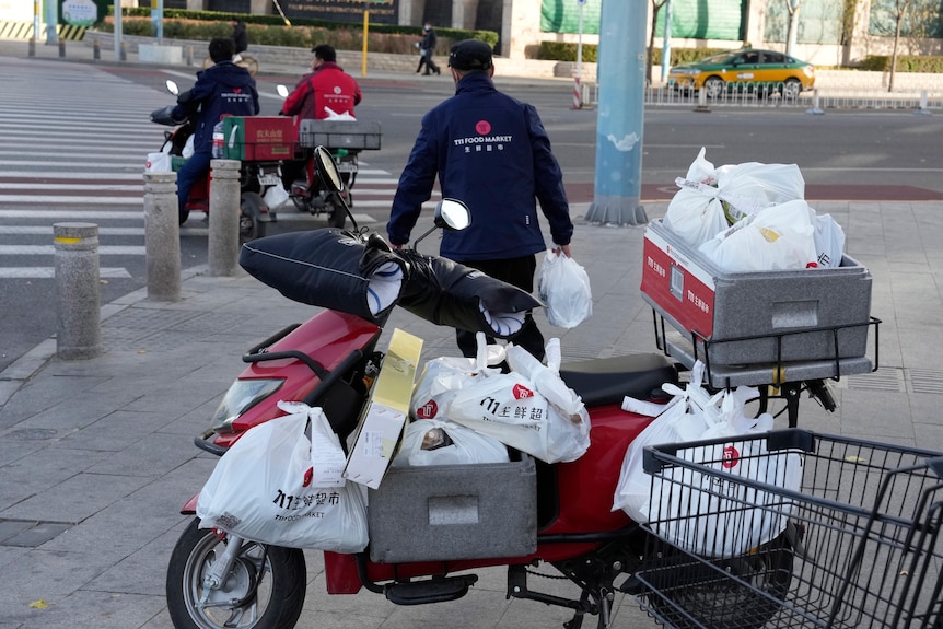 A motor bike covered in grocery bags with a person carrying bags in the background