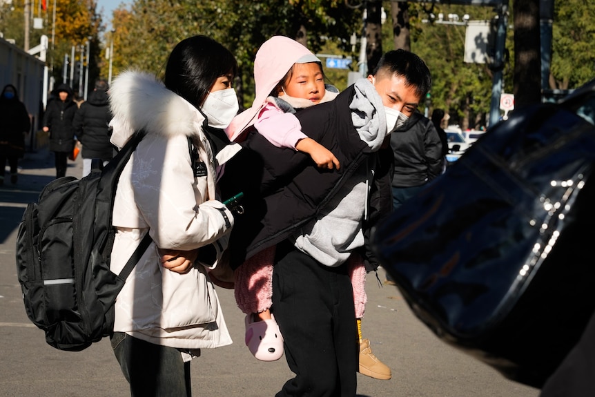 A man carries a child as he approaches a car.
