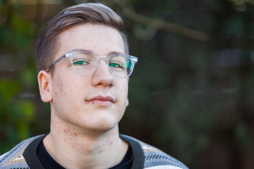 A head and shoulder portrait of a boy wearing glasses with clear rims.