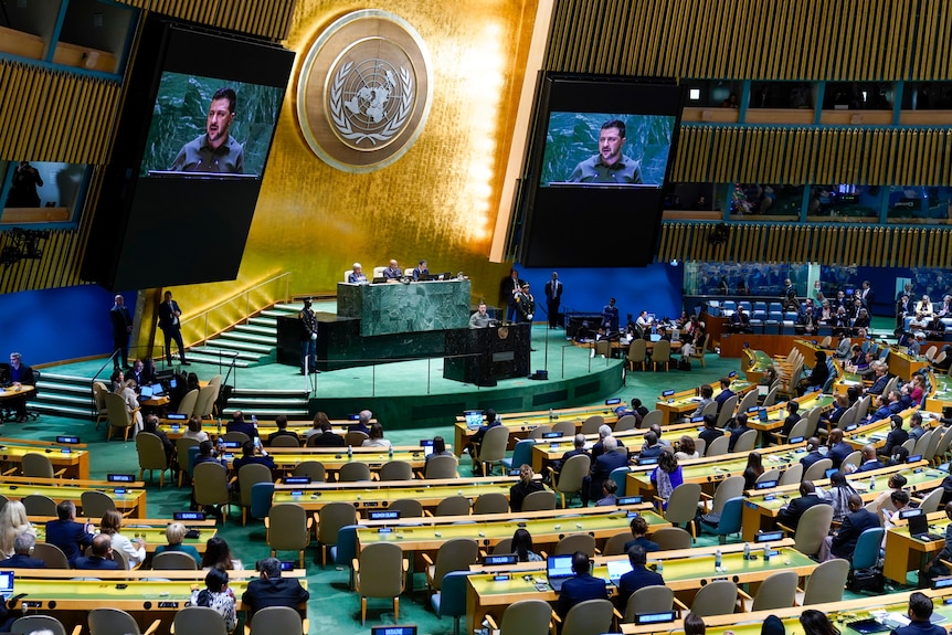 UN hall with Zelenskyy speaking projected on two screens on stage. 