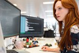 a redheaded woman at a computer looking at coding