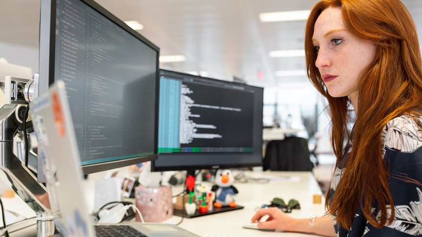 a redheaded woman at a computer looking at coding