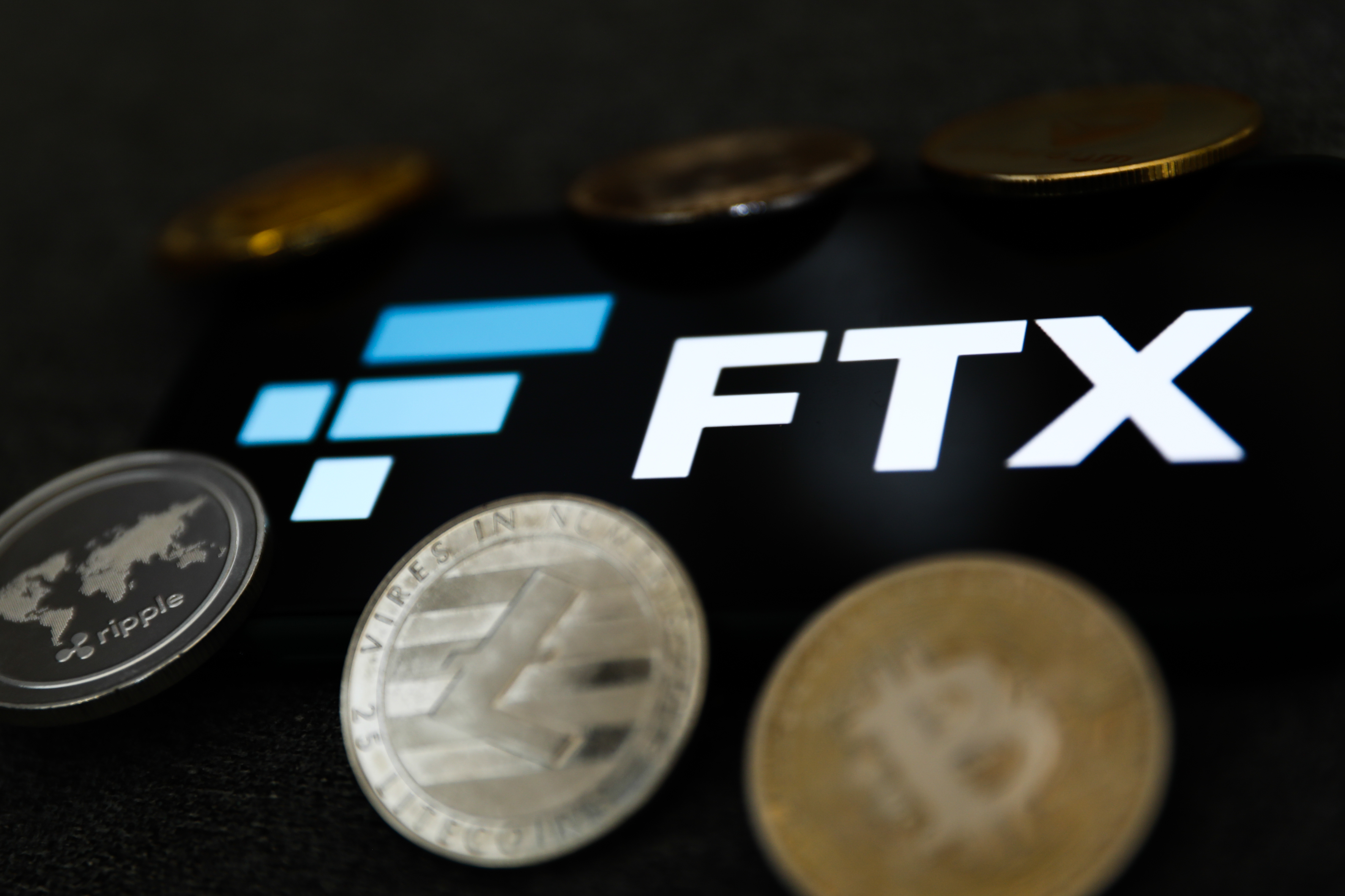手机屏幕上显示的 FTX 徽标和加密货币硬币的表示。