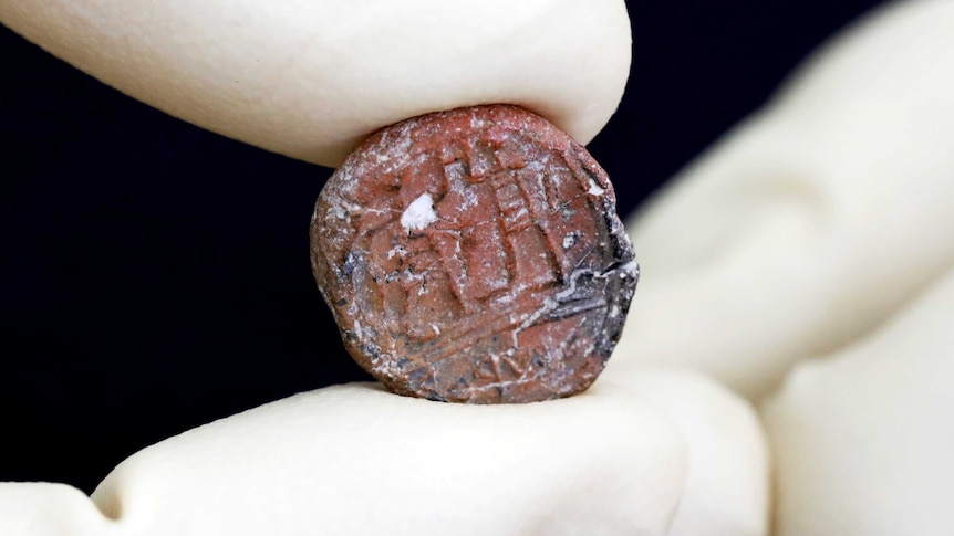 A close-up photograph of a coin-sized ancient seal.