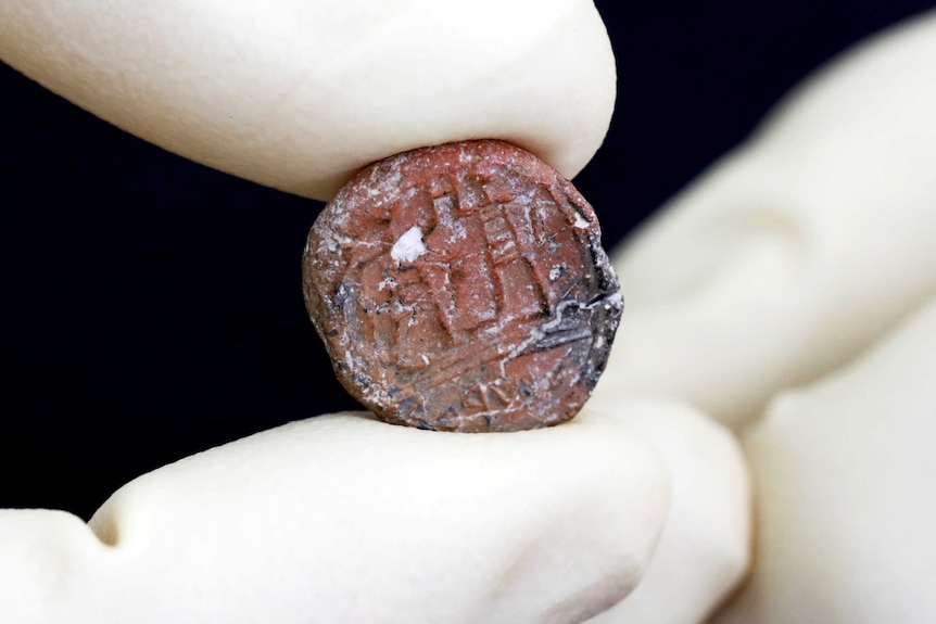 A close-up photograph of a coin-sized ancient seal.