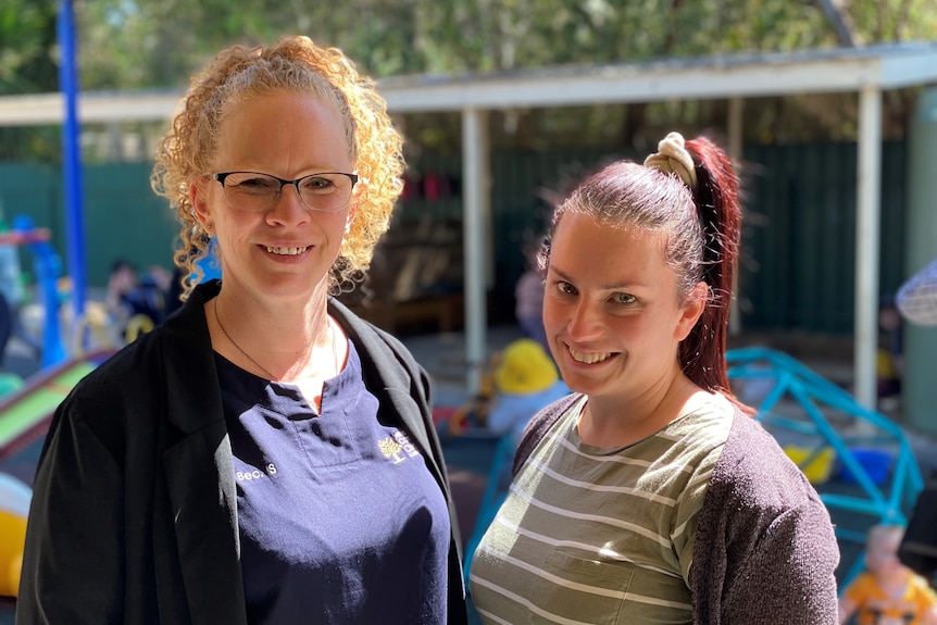 Two women smiling with a childcare centre in the background