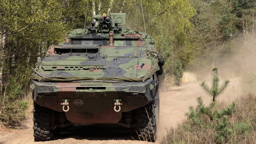A Boxer CRV combat military vehicle drives on a dirt road at speed.