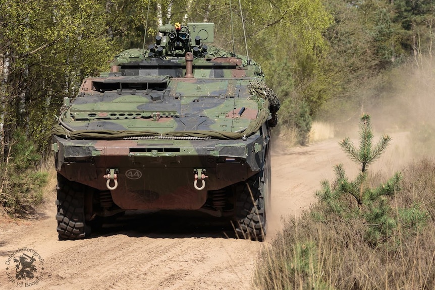 A Boxer CRV combat military vehicle drives on a dirt road at speed.