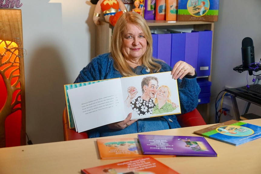 A woman sitting down at a desk holding up a childrens book