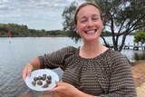 A woman stands next to a river holding a plate filled with alive snails