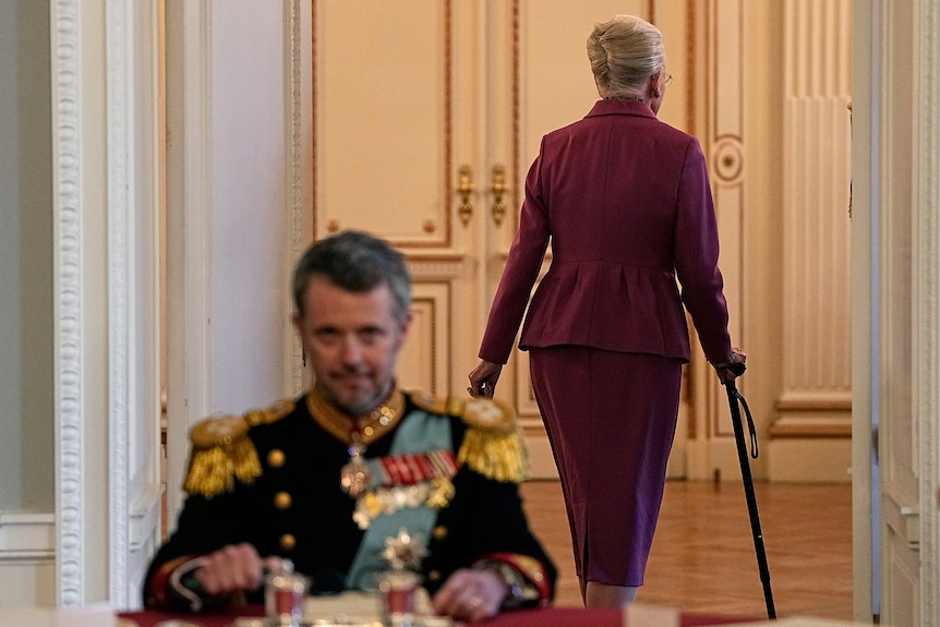 A woman leaves a room while a man sits at a table