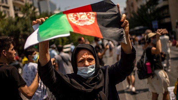 A woman in a hijab holds up the Afghan flag on a street