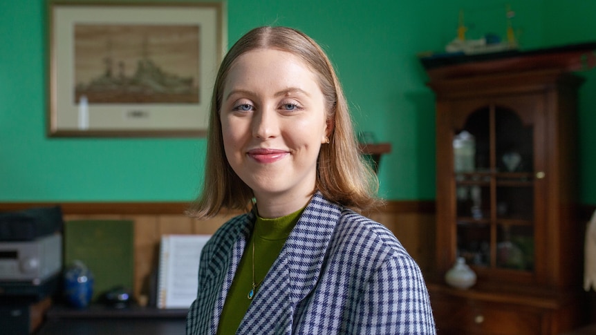 A young person wearing a blazer smiles at the camera.