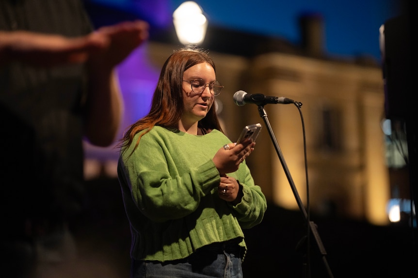 A young girl speaks at a candlelight vigil, standing behind a microphone.
