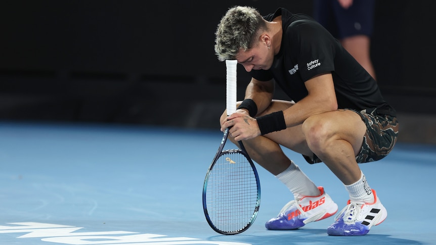 Thanasi Kokkinakis crouches down and leans his head on his racquet