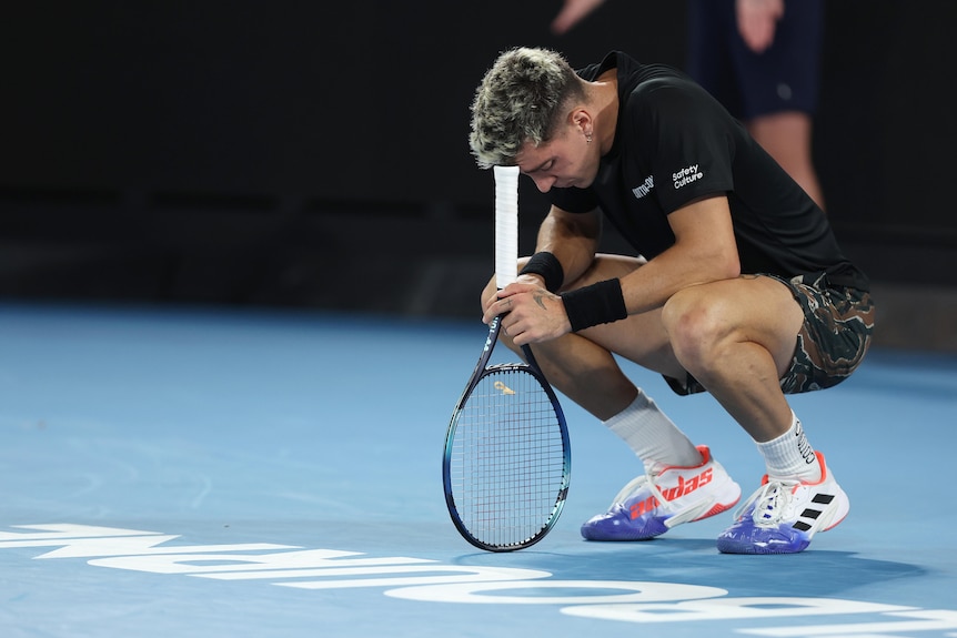Thanasi Kokkinakis crouches down and leans his head on his racquet