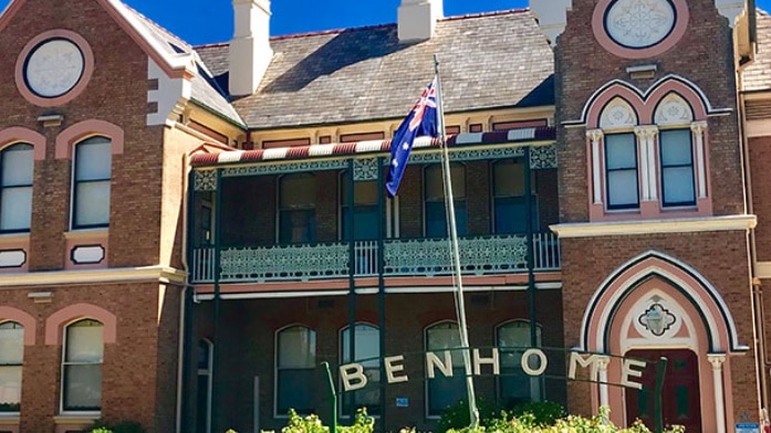 An ornate two-storey building with decorative windows and verandahs, with a Benhome sign at the front.