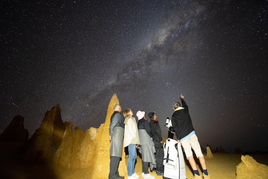 A group of people look up at the stars, with rocky outcrops in the background.