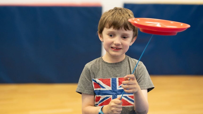 A little boy smiles as he spins a plate on a stick