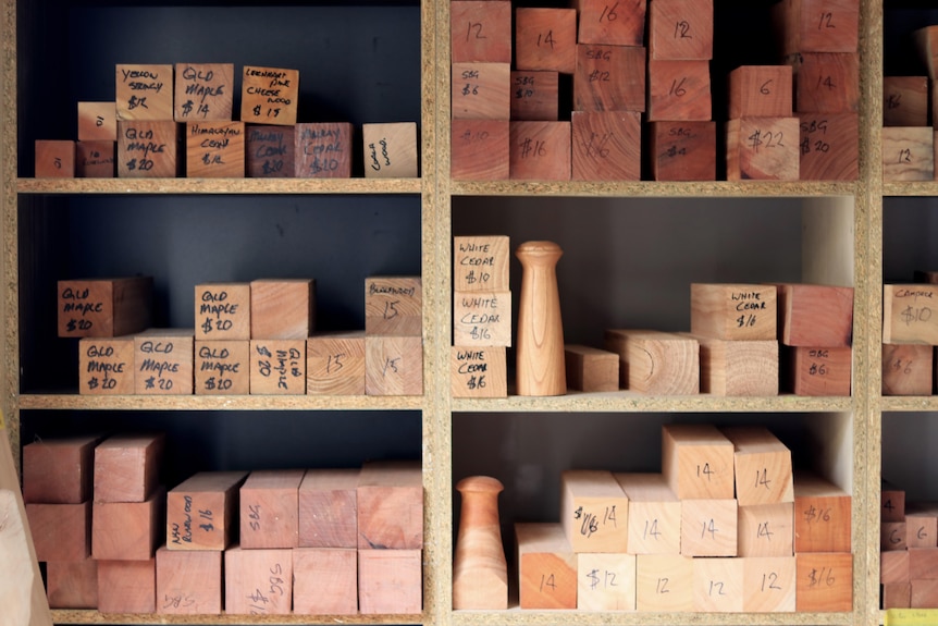 Planks of rectangular wood are stacked in shelves with species and prices written on their ends.