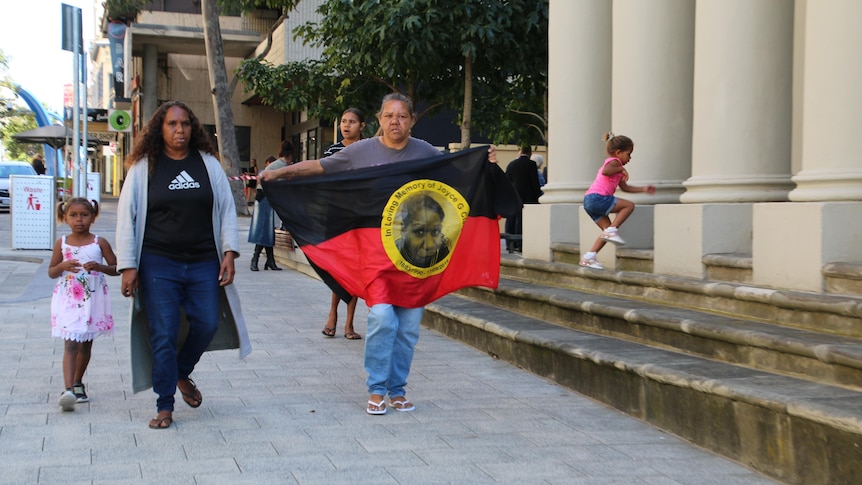 Two Aboriginal woman are walking with a girl, holding a flag