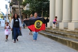 Two Aboriginal woman are walking with a girl, holding a flag