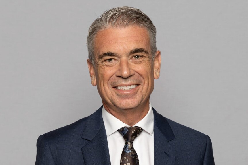 Michael Health smiles in a studio portrait shot while wearing a suit and tie