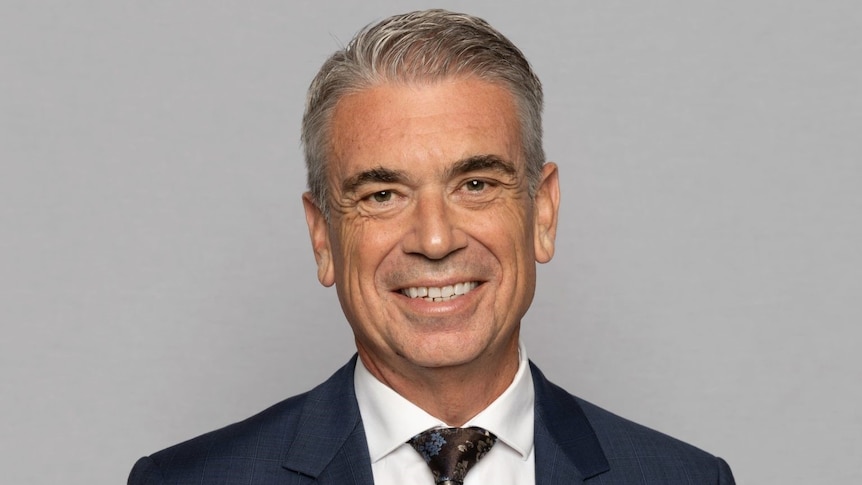 Michael Health smiles in a studio portrait shot while wearing a suit and tie