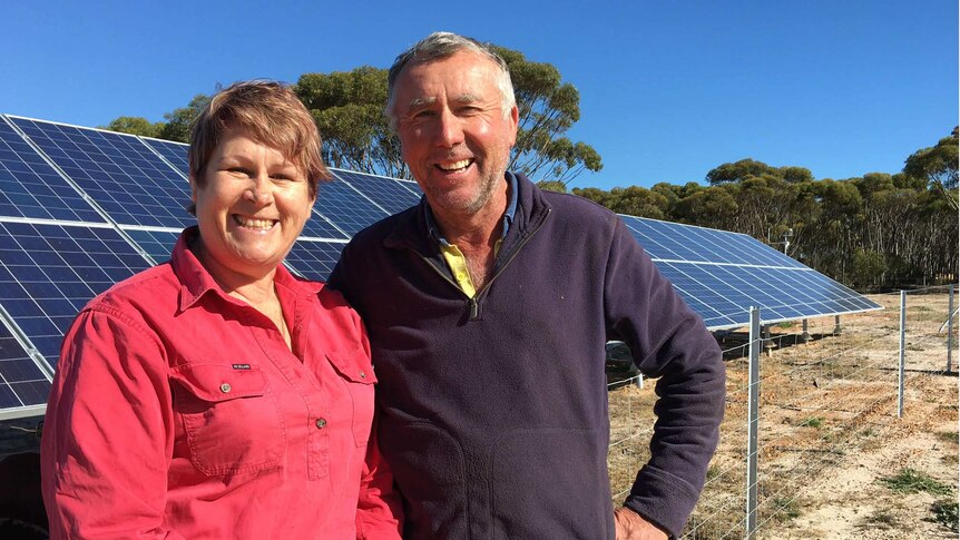 Ros and Bernie stand in front of solar panels on their farm.