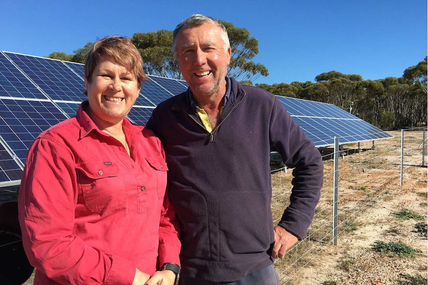 Ros and Bernie stand in front of solar panels on their farm.