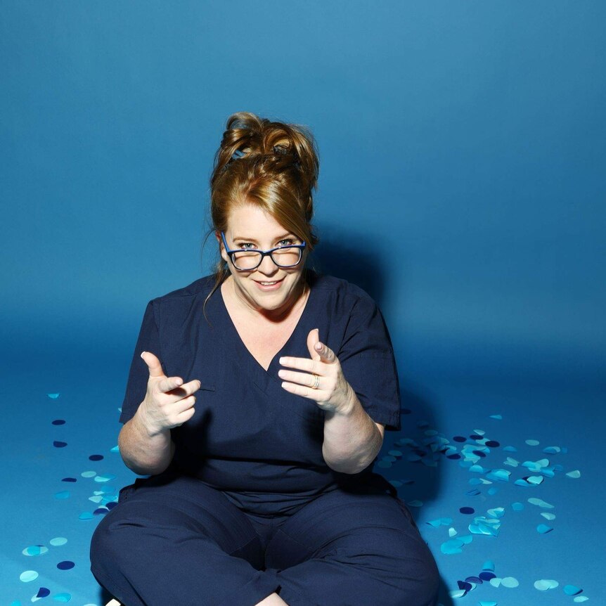 woman wearing nurses scrubs and glasses sitting and pointing fingers
