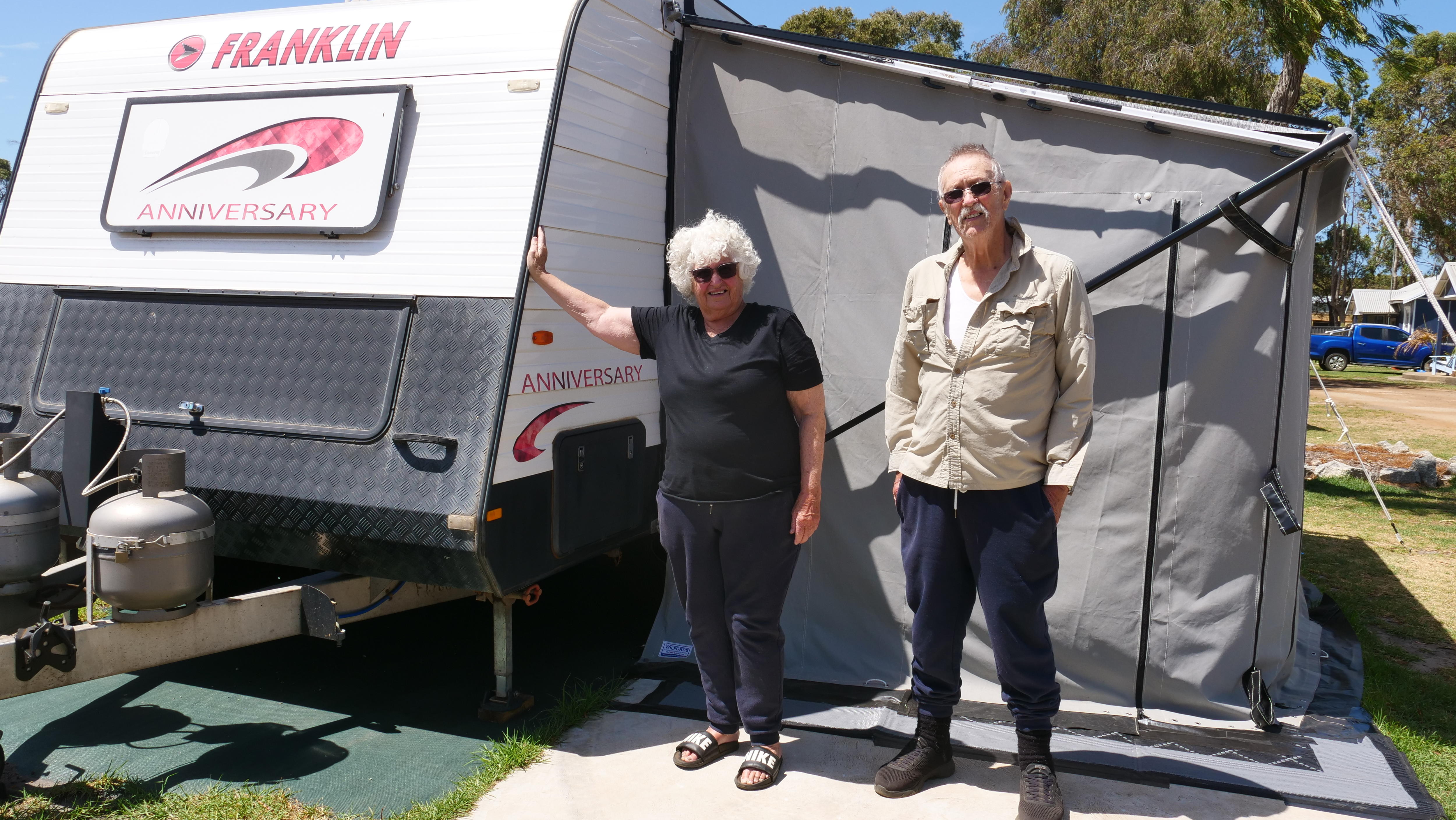 Plano medio de dos personas paradas delante de una caravana.