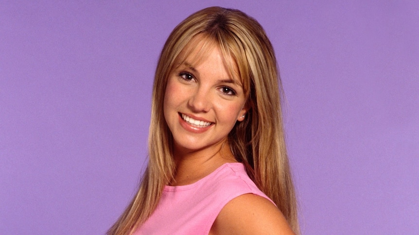 US pop star Britney Spears as a teenager wearing a pink shirt standing in front of a purple background