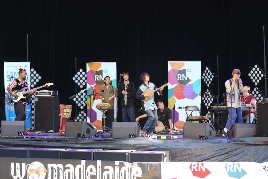 Wide shot stage with musicians playing and RN signage in background.