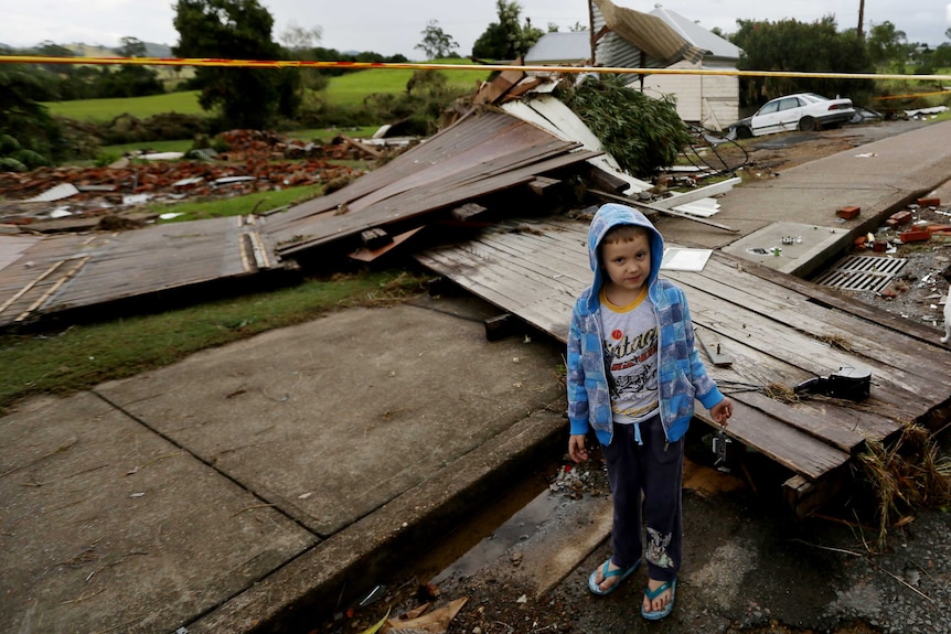 A young boy stands in front of a house destroyed by last year's storm that also hit the Hunter's Dungog region.