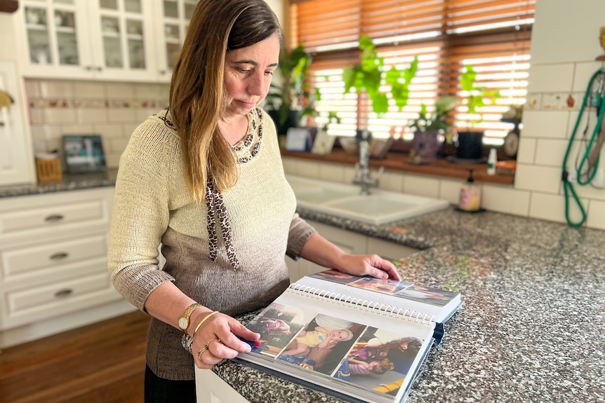 Lee-Anne Daffy flips through a photo album while standing at her kitchen bench.