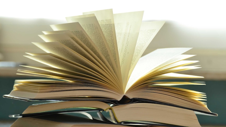 Open books stacked on top of one another, the top one with fanning pages.