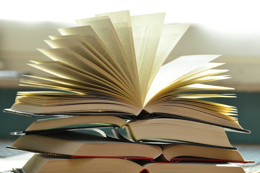 Open books stacked on top of one another, the top one with fanning pages.