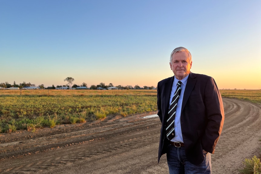A man in a suit standing on a block of land in outback Queensland with the sun setting behind him. 
