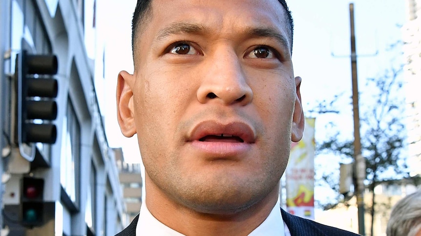 Israel Folau wearing a suit and looking up in a media scrum.