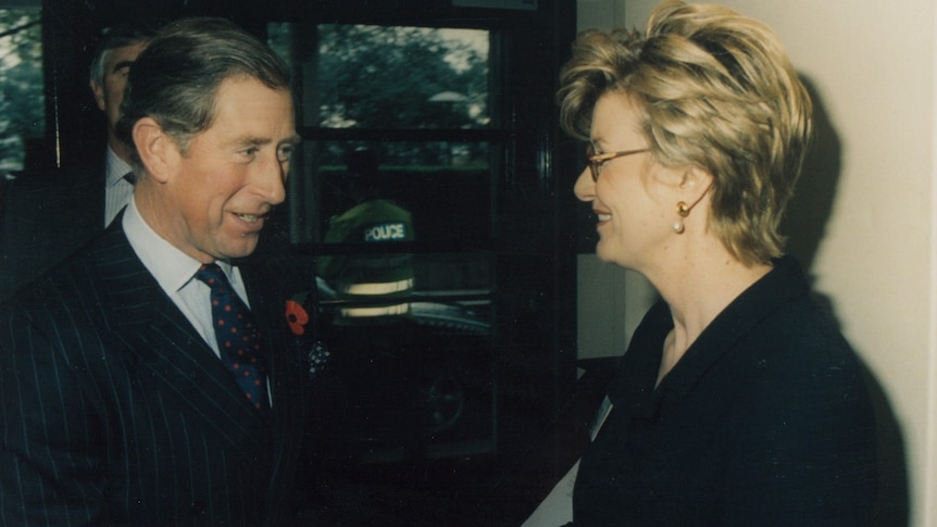 A man in a suit shakes hands with a blonde woman in glasses 