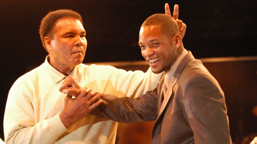 Boxing legend Muhammad Ali gestures behind the head of actor Will Smith