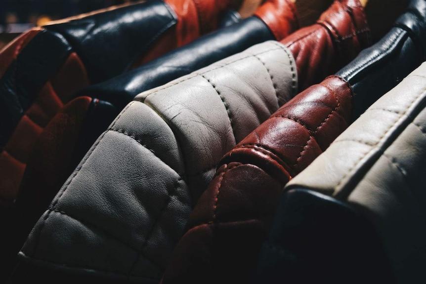 Close up of leather jackets in brown, black and grey on wooden coat hangers.