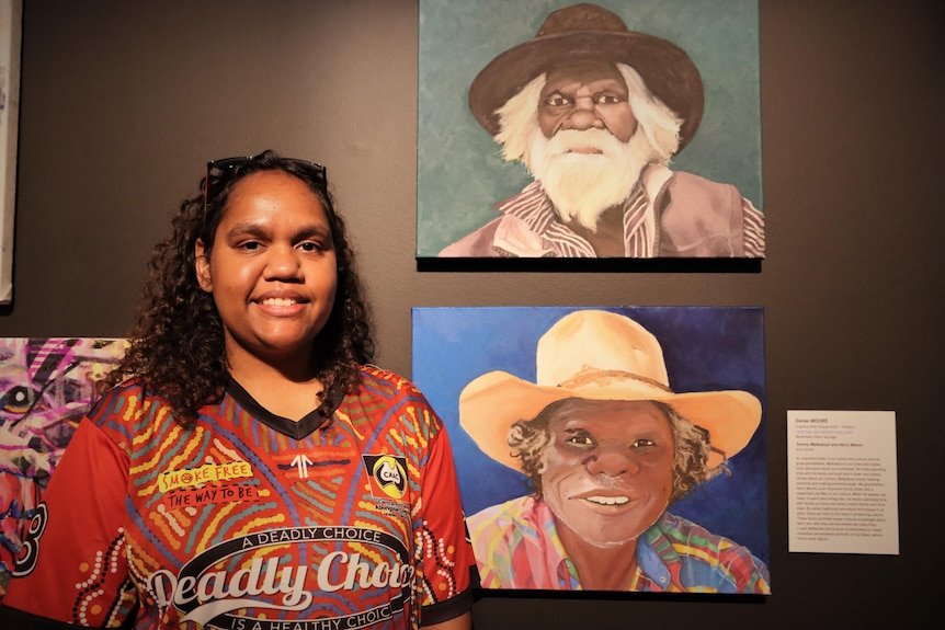 A woman stands in front of two portrait paintings.