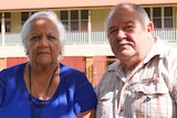 An elderly south sea islander woman sits next to an elderly white man. They look upset 